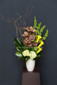 This elegant flower arrangement features bronze orchids, green molucca balm, yellow calla lilies, white hydrangea, tropical leaves, leather fern and contorted willow.